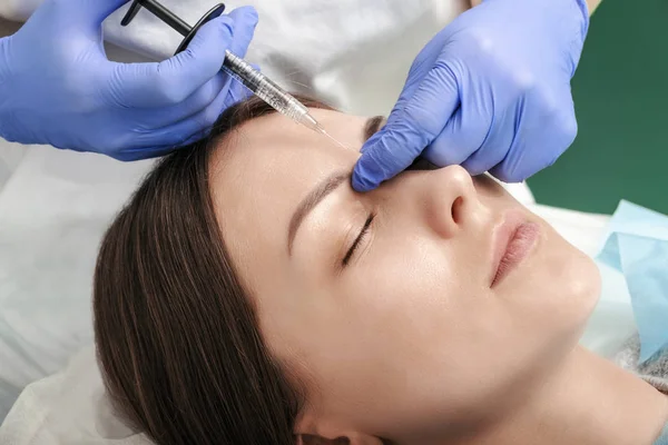 Güzellik güzel bir kadının yüzünde kaşları arasında enjeksiyonlar yapar. Mimik kırışıklıklarının düzeltilmesi. Kozmetoloji. Tıp merkezinde kozmetik prosedürler