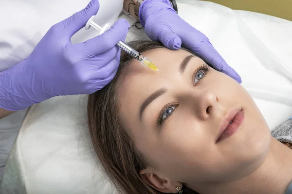 Um cosmetologista faz procedimentos anti-envelhecimento, uma injeção de rosto para suavizar rugas entre as sobrancelhas na pele do rosto de uma mulher bonita e jovem. Correção de rugas mímicas . — Fotografia de Stock