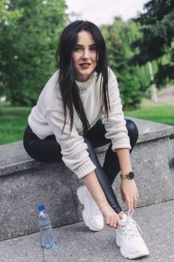 Güzel esmer kadın ayakkabılarına ayakkabı bağcığı bağlamak için oturdu. fitness konsepti