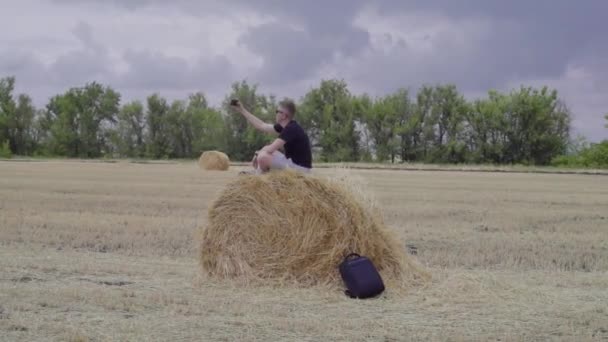 Мандрівник приймає селфі, сидячи на тюці сіна — стокове відео