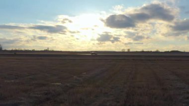 Gün batımında sahada yolda havadan görüntülenen araba sürmek. Drone profilinde araba izler.