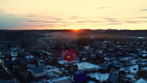 Luchtfoto van het dorp in de winter bij zonsondergang. De drone vliegt laag over de huizen. — Stockvideo