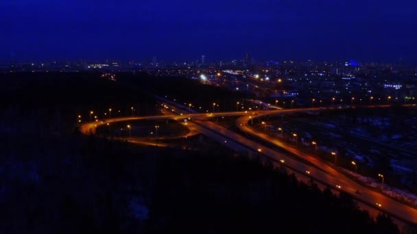 Widok z lotu ptaka na duże, oświetlone skrzyżowanie drogowe w nocy pełne samochodów i ciężarówek. — Wideo stockowe
