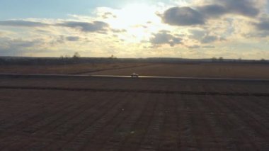 Gün batımında sahada yolda havadan görüntülenen araba sürmek. Drone profilinde araba izler.