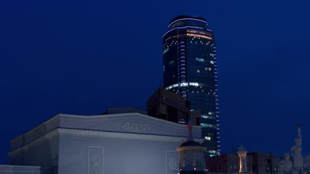 Vista aérea del centro de negocios que aparece detrás del edificio en el momento en que el dron vuela por la noche . — Vídeos de Stock