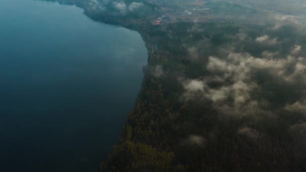 Vue aérienne d'un grand lac et d'un rivage avec forêt dans le brouillard et nuages bas.