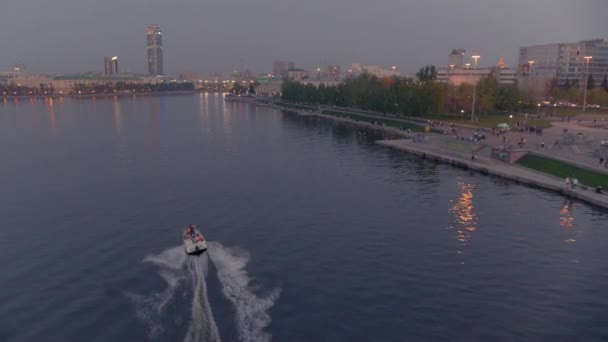 An aerial view of a boat that floats on a river in the city centre at sunset — Stock Video