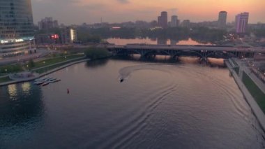 Gün batımında şehir merkezinde bir nehirde yüzen bir teknenin hava görüntüsü.