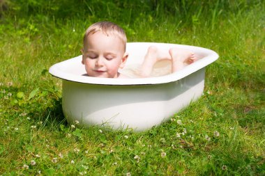 Mutlu ve huzurlu 3 yaşındaki çocuk beyaz küvette açık havada güneşli yaz günü ve sıcak hava banyo