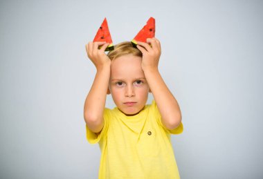 Frolicsome kafkas 5 yaşındaki erkek çocuk boynuzları, inatçılık kavramı olarak başının üzerinde kırmızı karpuz iki adet tutan sarı t-shirt.