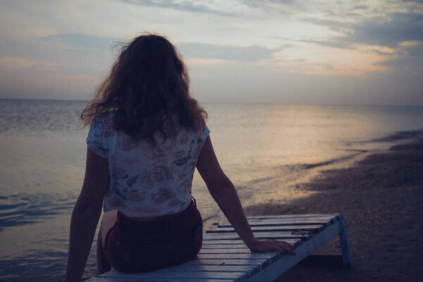 the girl sits on a bench on the beach and looks into the distance
