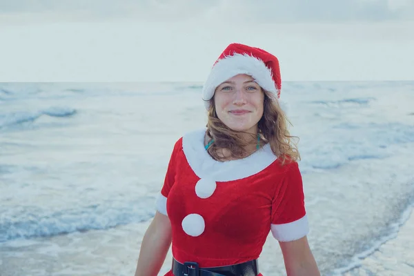 女孩装扮成圣诞老人站在海滩或海洋 圣诞节旅程的概念 新年快乐 圣诞愉快 — 图库照片