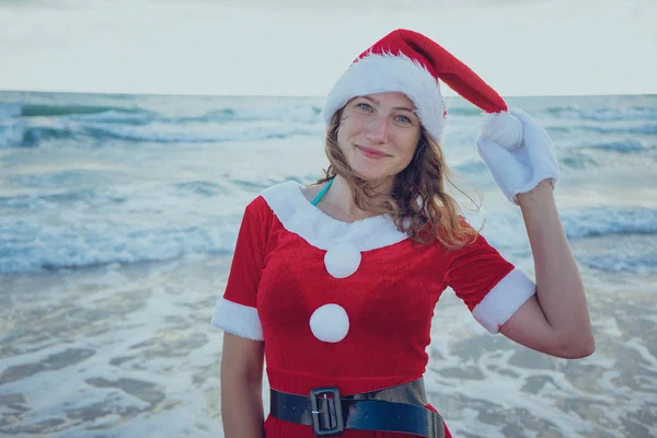 サンタ クロースに扮した女の子ビーチまたは海の上に立って クリスマスへの旅のコンセプトです メリー クリスマスと新年あけましておめでとうございます — ストック写真