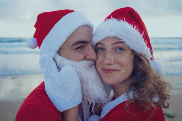 快乐的情侣在海滩上漫步圣诞老人的服装 圣诞节假期的概念 — 图库照片