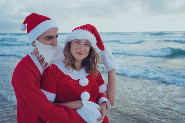 快乐的情侣在海滩上漫步圣诞老人的服装 圣诞节假期的概念 — 图库照片