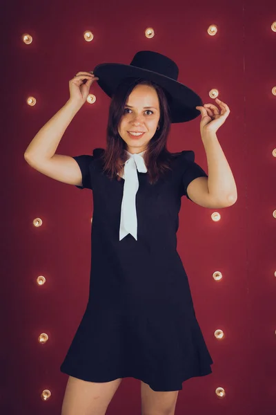 Девушка Черном Платье Черной Шляпе Позирует Красном Фоне — стоковое фото