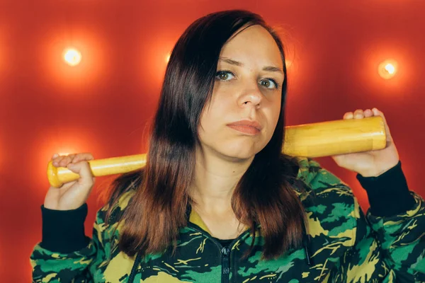 Young pretty girl with baseball bat, girl with bat. a girl or criminal holding a baseball bat in her hand on a red background. Sports and training