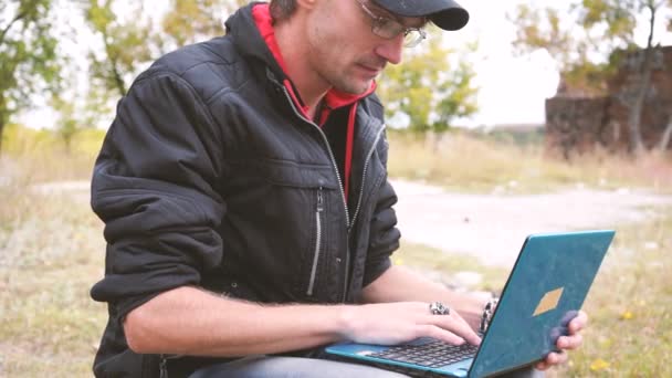 ハンサムな若い男が 屋外でノート パソコンを使用しています 学生は 快適な雰囲気の中屋外でノート パソコンを研究に焦点を当てた リモート作業コンセプト — ストック動画