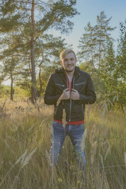 Deri ceketli bir sakallı bir genç adam şehirde Park yürür. duygusal bir öğrenci portresi. sokak tarzı. taze hava güneşli bir yaz ormanda bir adam girer.