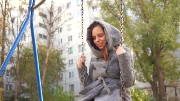 ブランコに揺れてコートの美しい少女 都市環境の背景に — ストック動画