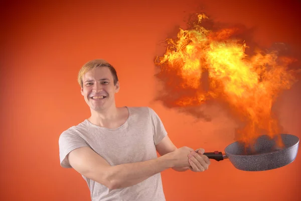 情绪化的家伙拿着一个煎锅在他的手中 在一个橙色的背景 燃烧的煎锅突然燃烧起来 这个概念 这家伙准备了一些特别的东西 — 图库照片