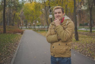 Zemin üzerine sarı ağaçları ile genç beyaz adam. Sonbahar sezonu zamanı. Bir öğrenci parkta yürüyor.