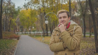 Zemin üzerine sarı ağaçları ile genç beyaz adam. Sonbahar sezonu zamanı. Bir öğrenci parkta yürüyor.