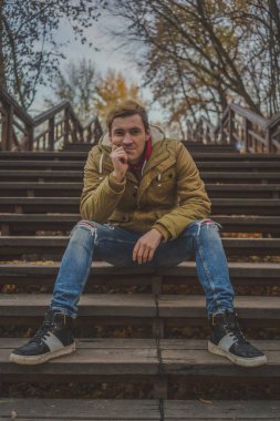 Zemin üzerine sarı ağaçları ile genç beyaz adam. Sonbahar sezonu zamanı. Bir öğrenci parkta yürüyor.