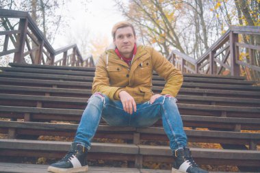 Zemin üzerine sarı ağaçları ile genç beyaz adam. Sonbahar sezonu zamanı. Bir öğrenci parkta yürüyor.