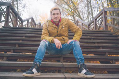 Zemin üzerine sarı ağaçları ile genç beyaz adam. Sonbahar sezonu zamanı. Bir öğrenci parkta yürüyor.