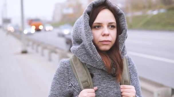 一个穿着灰色外套的年轻女孩走在马路上的栅栏附近 — 图库视频影像
