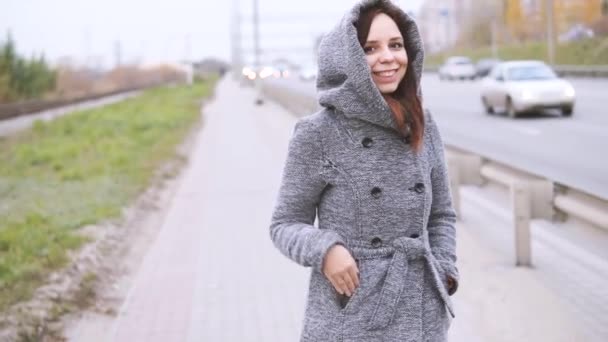 道路フェンスの近く歩く秋の灰色のコートを着た少女 — ストック動画