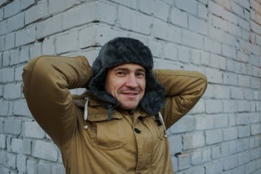 Cap güzelliğini ile mutlu yakışıklı genç adam. Kürk şapka genç adam. bulutlu bir günde sokakta duran genç bir adam. duygusal bir öğrenci portresi. sokak stili