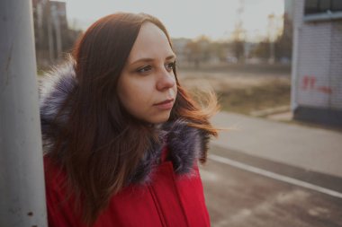 Bulutlu bir günde dışında poz bir kırmızı ceketli mutlu güzel genç kız. duygusal bir öğrenci portresi. sokak stili