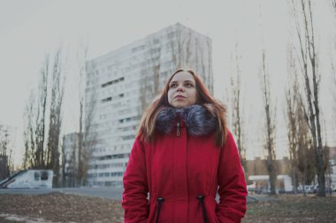Bulutlu bir günde dışında poz bir kırmızı ceketli mutlu güzel genç kız. duygusal bir öğrenci portresi. sokak stili