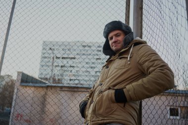 Cap güzelliğini ile mutlu yakışıklı genç adam. Kürk şapka genç adam. bulutlu bir günde sokakta duran genç bir adam. duygusal bir öğrenci portresi. sokak stili