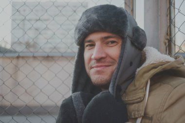 Cap güzelliğini ile mutlu yakışıklı genç adam. Kürk şapka genç adam. bulutlu bir günde sokakta duran genç bir adam. duygusal bir öğrenci portresi. sokak stili