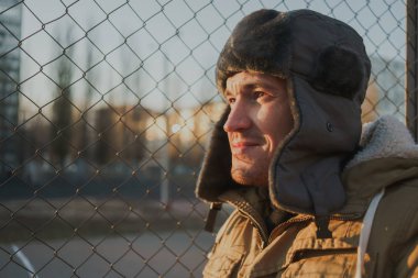 Cap güzelliğini ile mutlu yakışıklı genç adam. Kürk şapka genç adam. bulutlu bir günde sokakta duran genç bir adam. duygusal bir öğrenci portresi. sokak stili