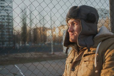 Cap güzelliğini ile mutlu yakışıklı genç adam. Kürk şapka genç adam. bulutlu bir günde sokakta duran genç bir adam. duygusal bir öğrenci portresi. sokak stili