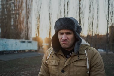 Cap güzelliğini ile mutlu yakışıklı genç adam. Kürk şapka genç adam. bulutlu bir günde sokakta duran genç bir adam. duygusal bir öğrenci portresi. sokak stili