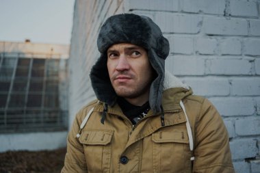 Cap güzelliğini ile mutlu yakışıklı genç adam. Kürk şapka genç adam. bulutlu bir günde sokakta duran genç bir adam. duygusal bir öğrenci portresi. sokak stili