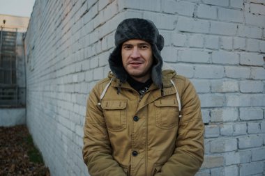 Cap güzelliğini ile mutlu yakışıklı genç adam. Kürk şapka genç adam. bulutlu bir günde sokakta duran genç bir adam. duygusal bir öğrenci portresi. sokak stili