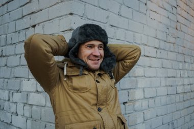 Cap güzelliğini ile mutlu yakışıklı genç adam. Kürk şapka genç adam. bulutlu bir günde sokakta duran genç bir adam. duygusal bir öğrenci portresi. sokak stili