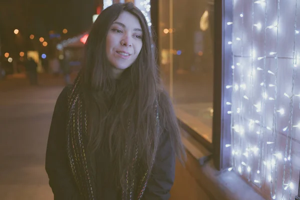 Girl Eastern looks, walking through the city at night, in the winter. Woman in winter jacket with scarf. Street style clothing