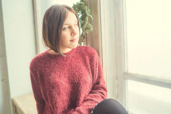 The girl sits on the window, the student looks thoughtfully. Model posing at the window. Concept: romance and longing