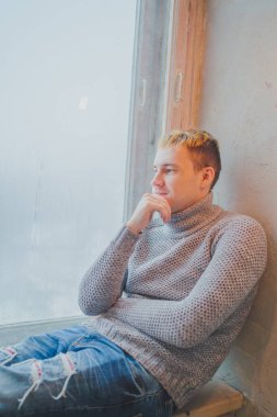 Yakışıklı olan büyük bir pencere arka pencere kenarında oturan. Adam hayal bir şey yönünde görünüyor.