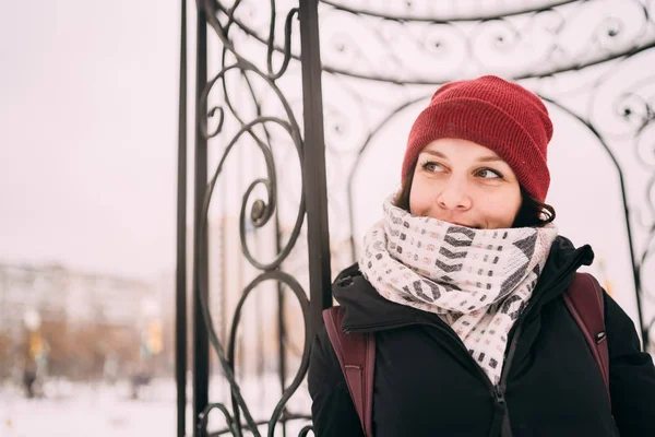 portrait of a beautiful blonde in a hat and scarf on the background of the city landscape in the cold season. girl walking down the street