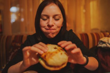Kadın yemek hamburger Fransız. Öğrenci portresi lokanta masada tüketmek. Kız önemsiz yemek yiyor. Lokanta daek arka plan üzerinde reklam. Öğrenci yarı bitmiş ürünler yiyor.