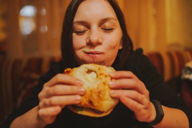 Kadın yemek hamburger Fransız. Öğrenci portresi lokanta masada tüketmek. Kız önemsiz yemek yiyor. Lokanta daek arka plan üzerinde reklam. Öğrenci yarı bitmiş ürünler yiyor.