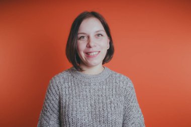 Genç kız sıcak gri süveterli kadın örme kazaklı kısa saç kesimi, metin için yer ile turuncu arka plan üzerinde poz